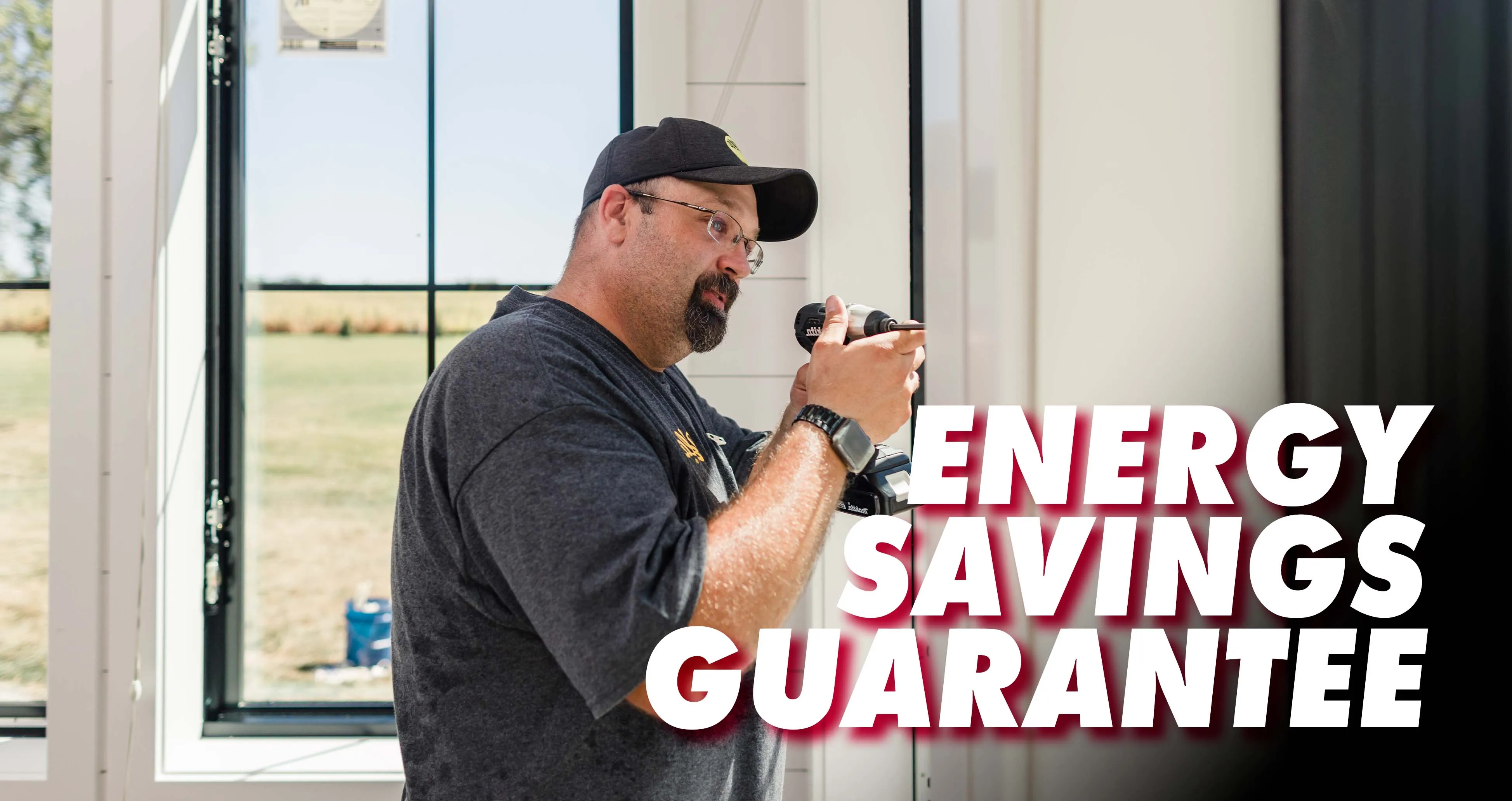 Man wearing a black cap and glasses using a power drill near a window with text Energy Savings Guarantee.